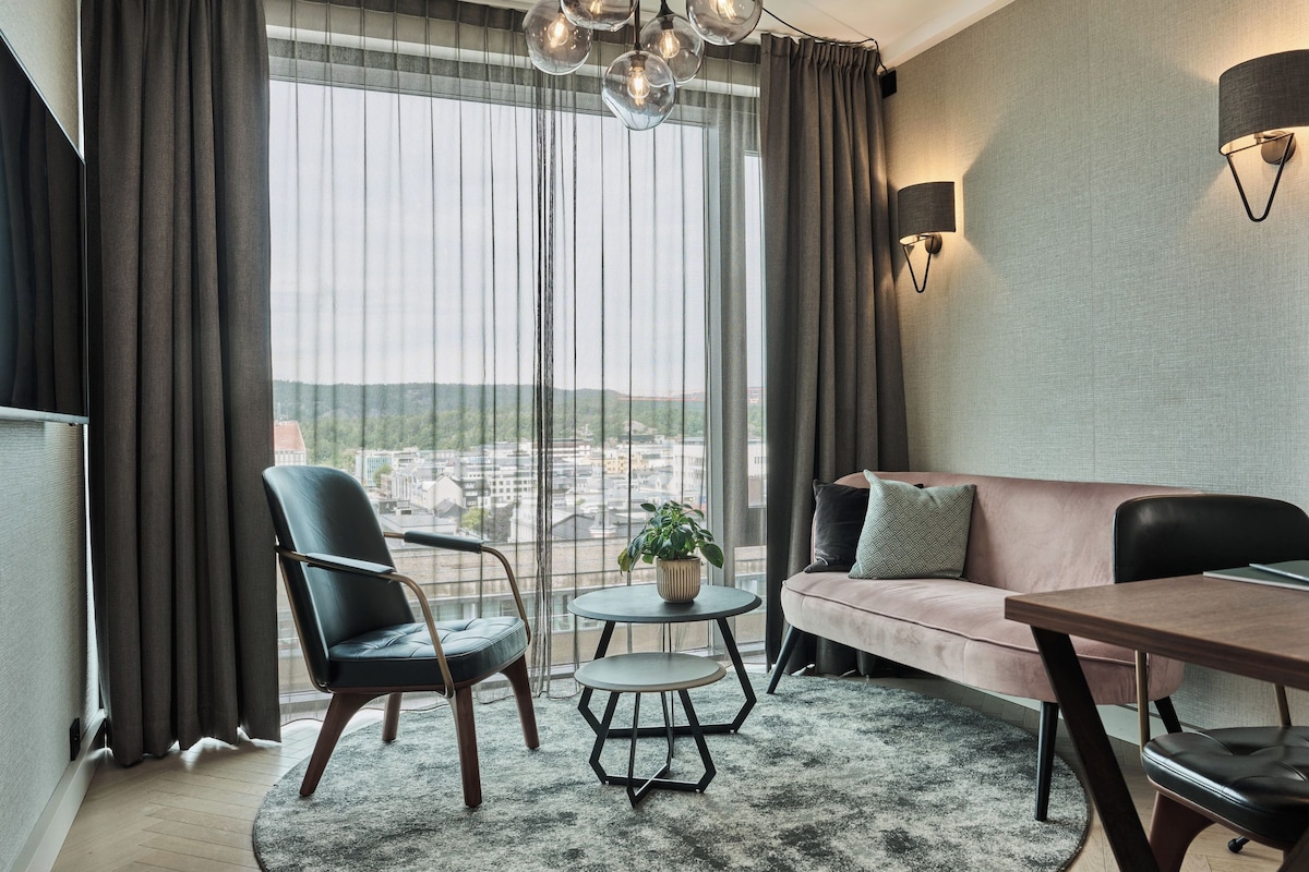 A modern living room with a sofa, two chairs, a small round table, and a potted plant.