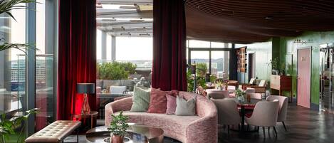 A spacious lobby with a modern design, featuring a mix of seating areas, a coffee bar, and a view of the cityscape through large windows.
