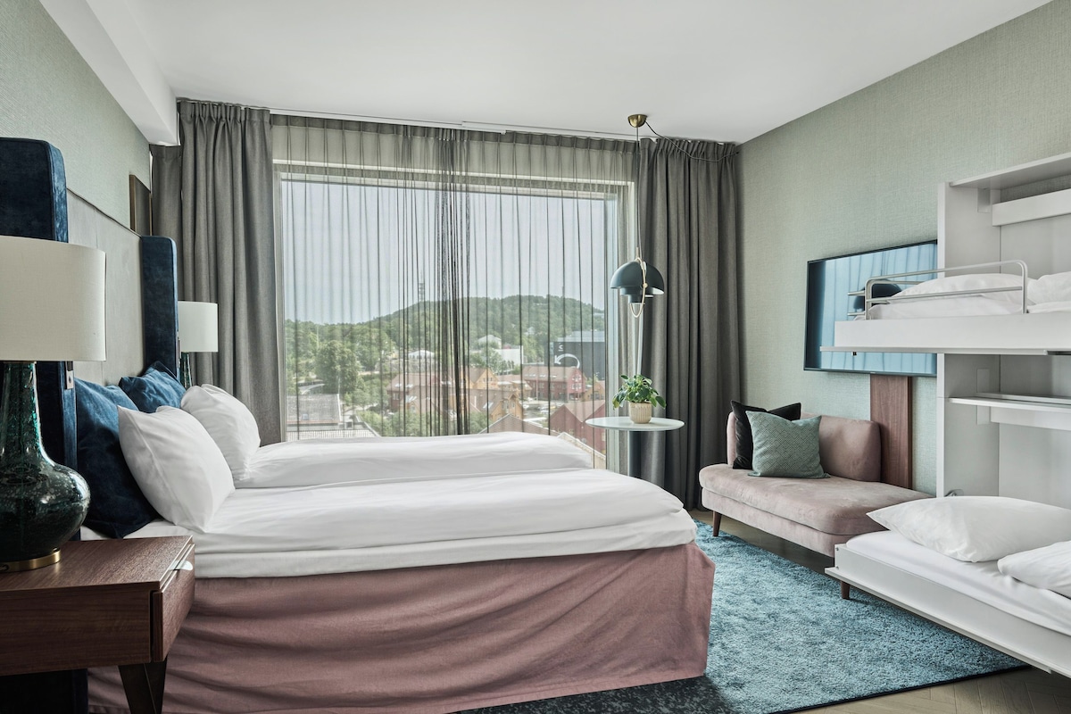 A hotel room with a large bed, a sofa, a desk, and a bunk bed.