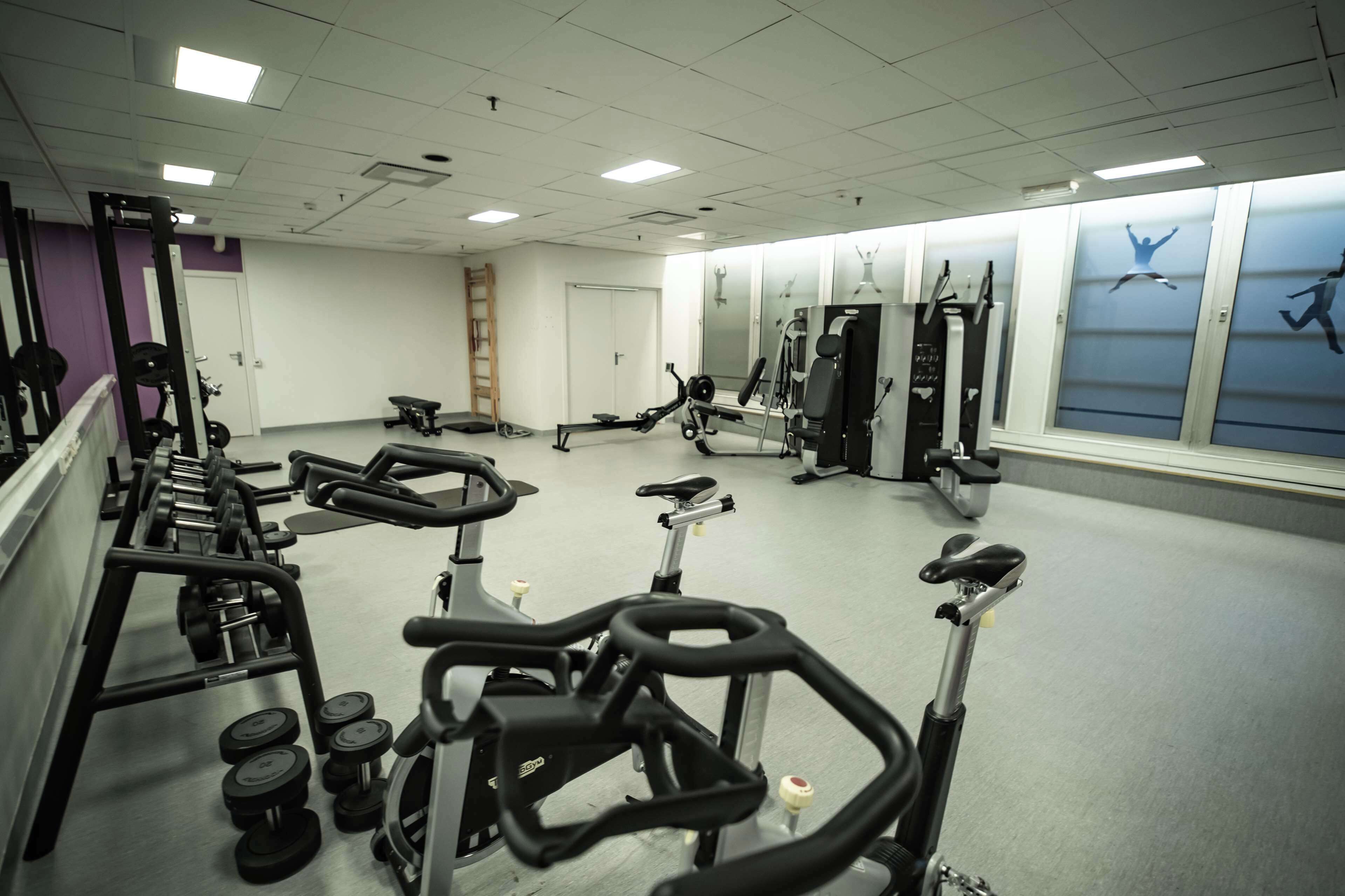 Un gimnasio con equipo de ejercicio, espejos y una pared decorada con motivos relacionados con el fitness.
