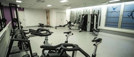 A gym with exercise equipment, mirrors, and a wall with fitness-themed artwork.