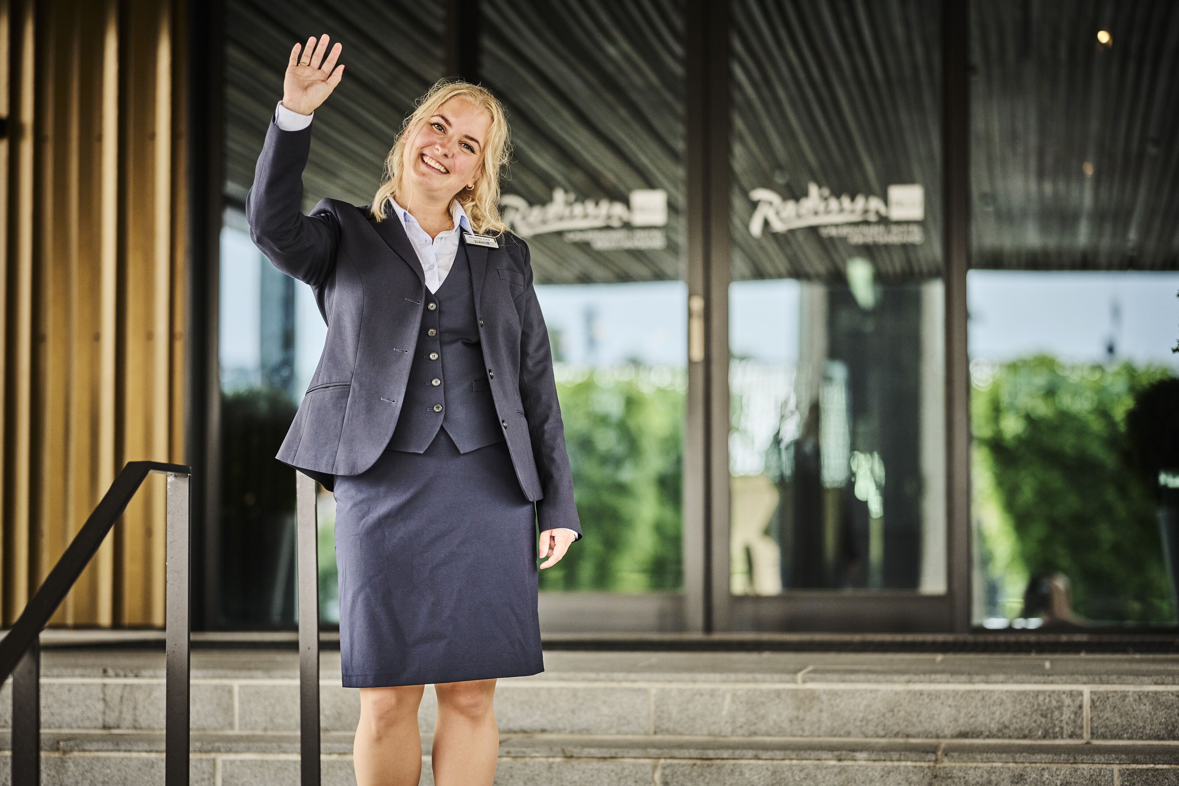 A person in business attire standing in front of a building with a sign that reads "Riviera."