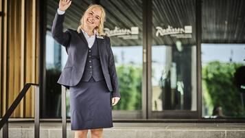 A person in business attire standing in front of a building with a sign that reads "Riviera."