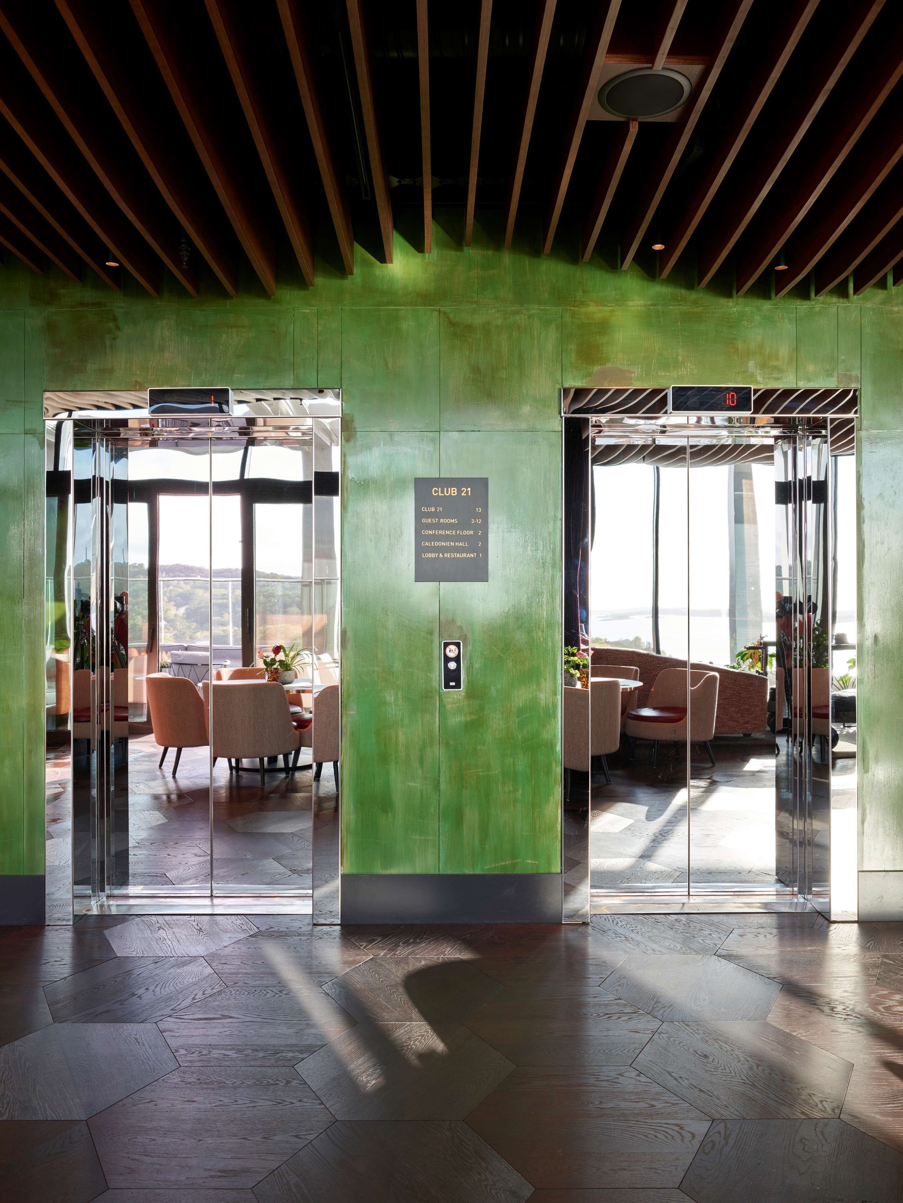 A modern elevator with a digital display, a sign indicating CLUB 21, and a view of a lounge area with seating and plants.