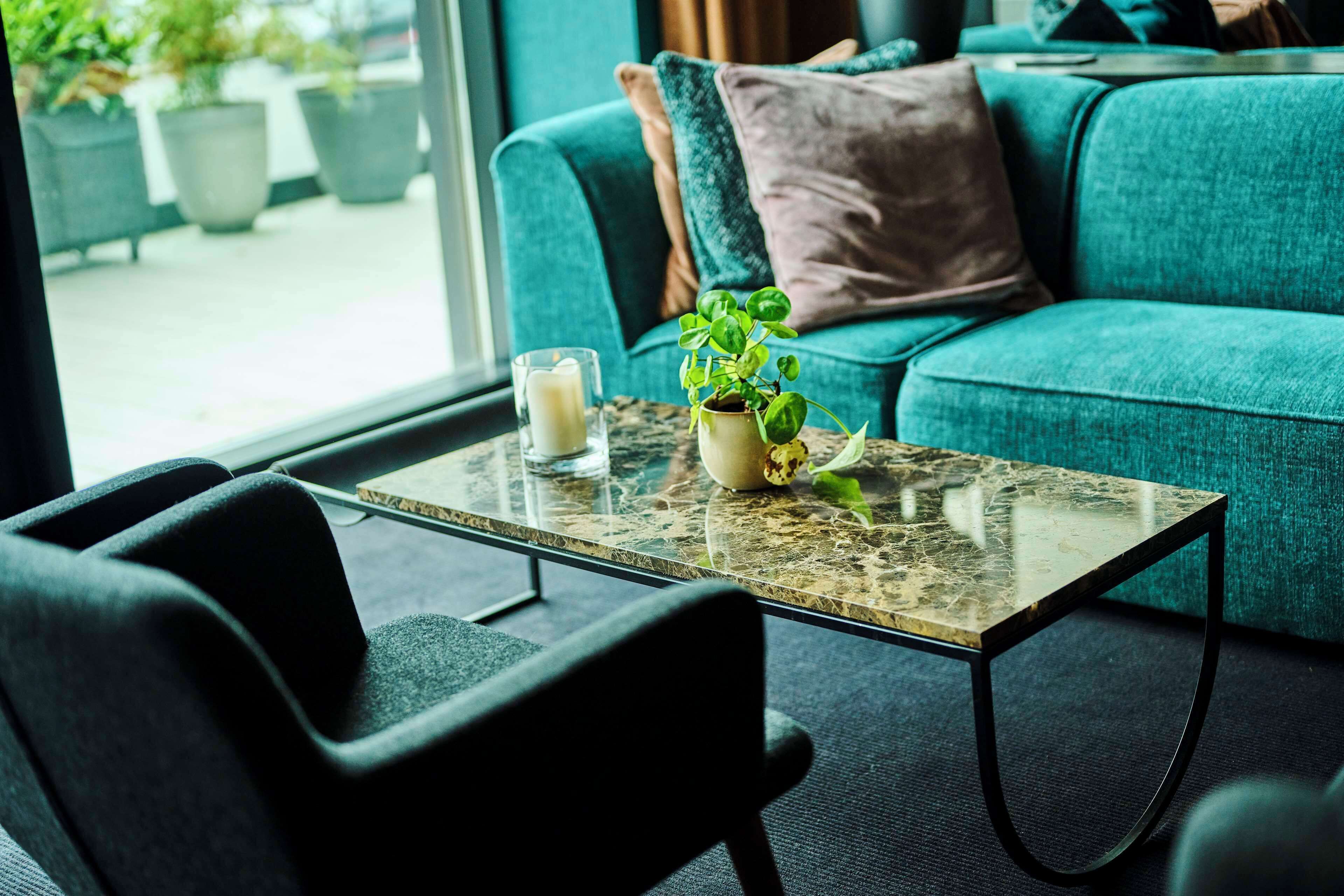 A modern room with a teal sofa, a glass coffee table with a plant, and a candle.