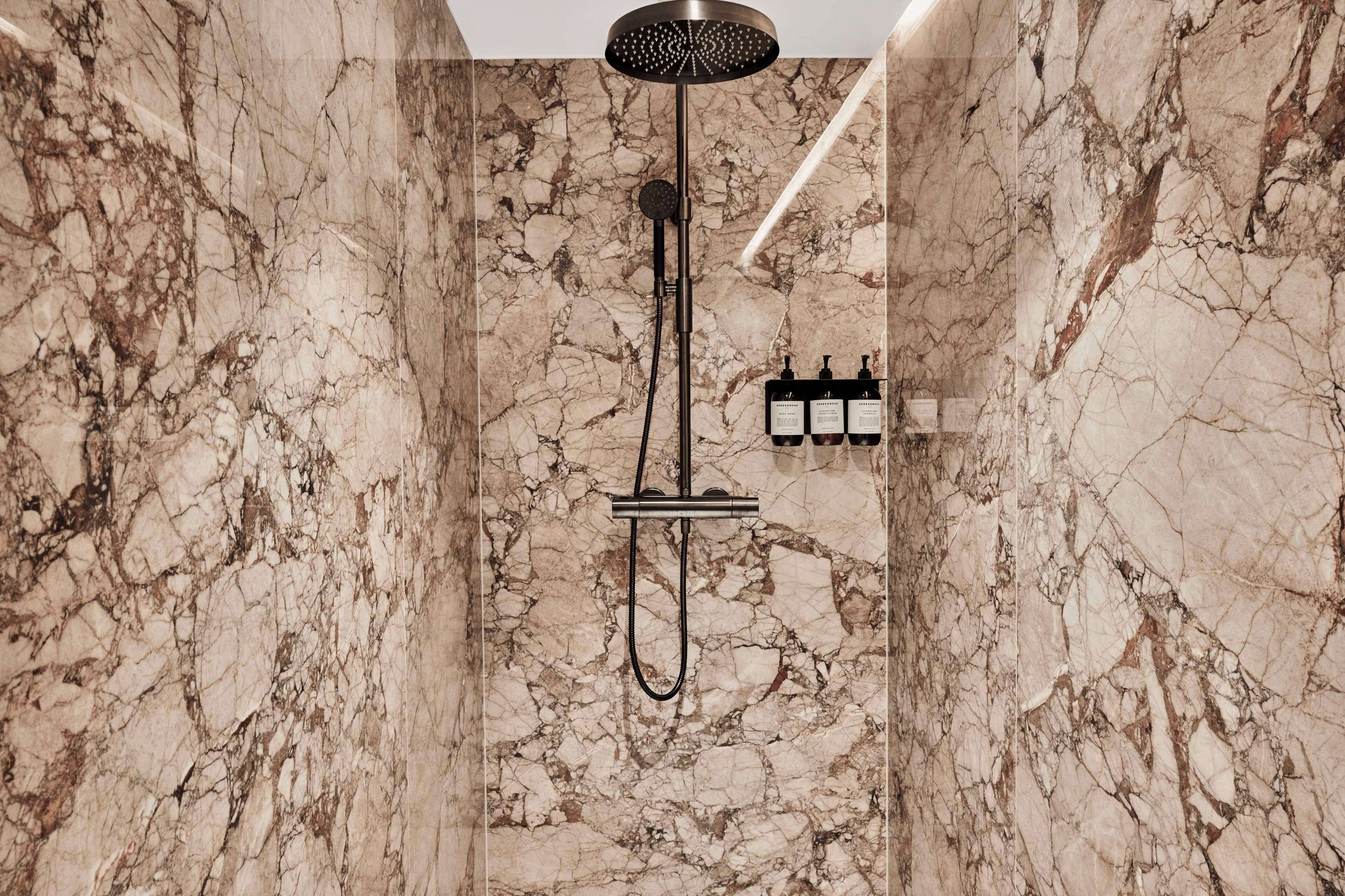 A modern bathroom with a marble wall, a showerhead, and a handheld shower attachment.