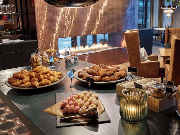 A breakfast buffet with pastries, a fire feature, and a cozy seating area. - Hotel Caledonien (Kristiansand)