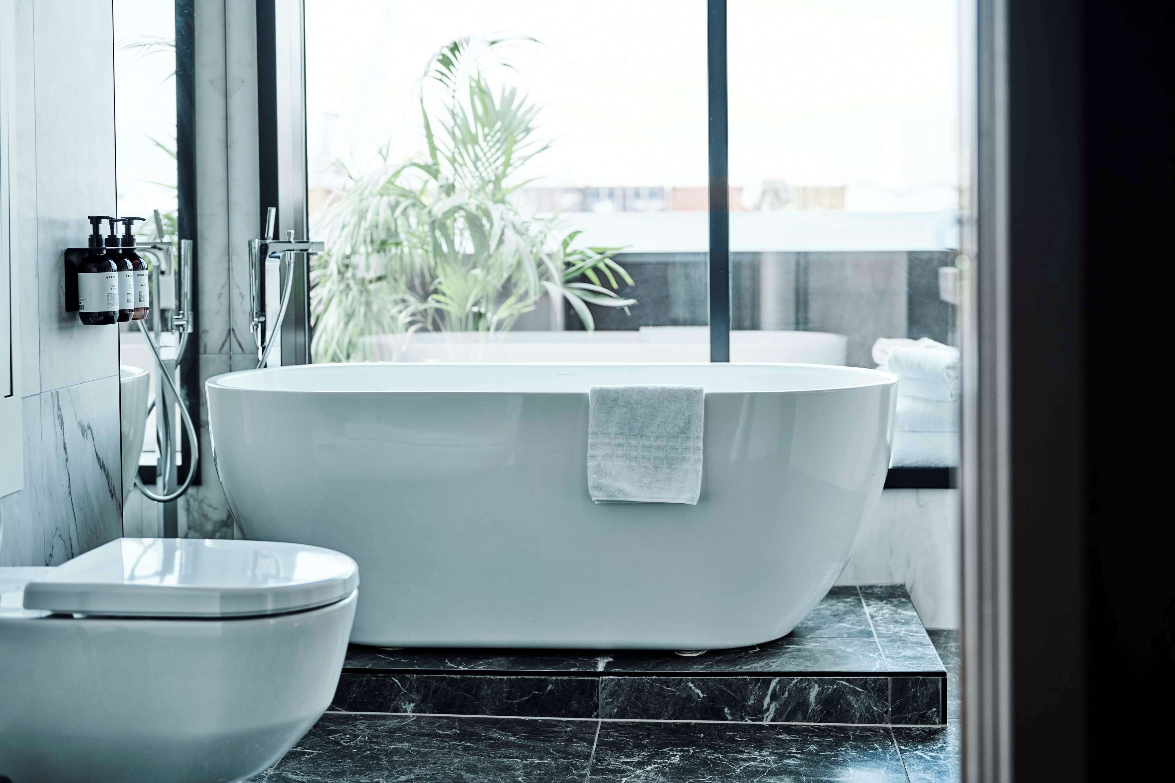 A modern bathroom with a freestanding bathtub, a toilet, and a large window providing a view of the outdoors.