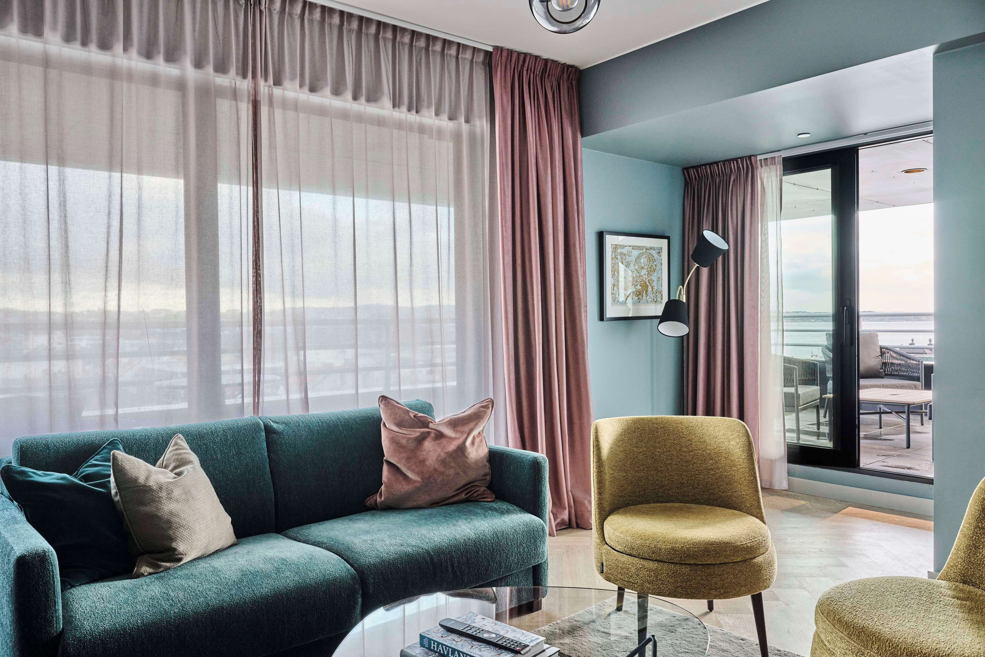 A modern living room with a teal sofa, a gold armchair, and a glass coffee table.