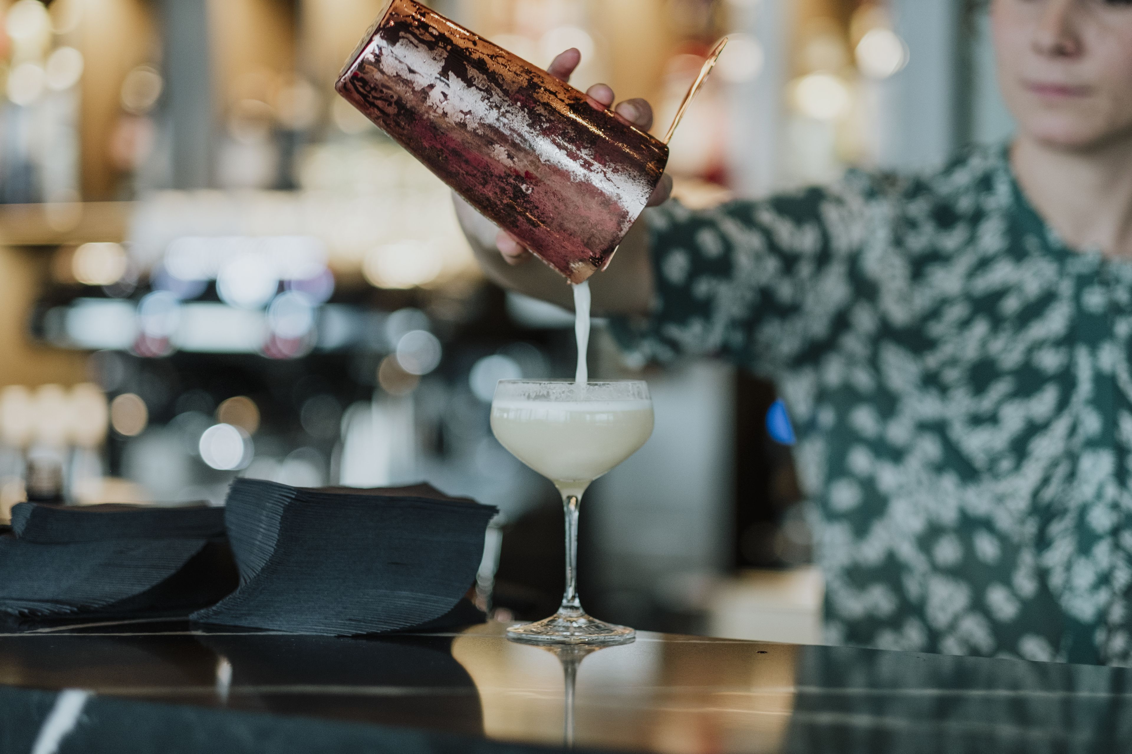 Une scène de bar où l’on verse un cocktail dans un verre.