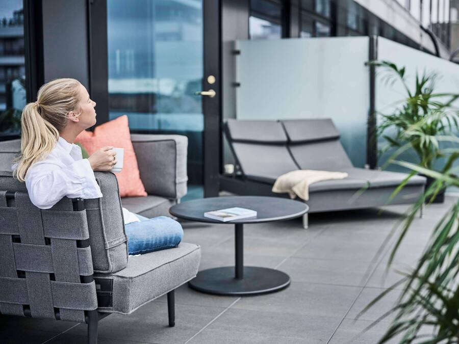 Un área de estar moderna al aire libre con un sofá, una silla de lounge, una mesita redonda y una planta en maceta.