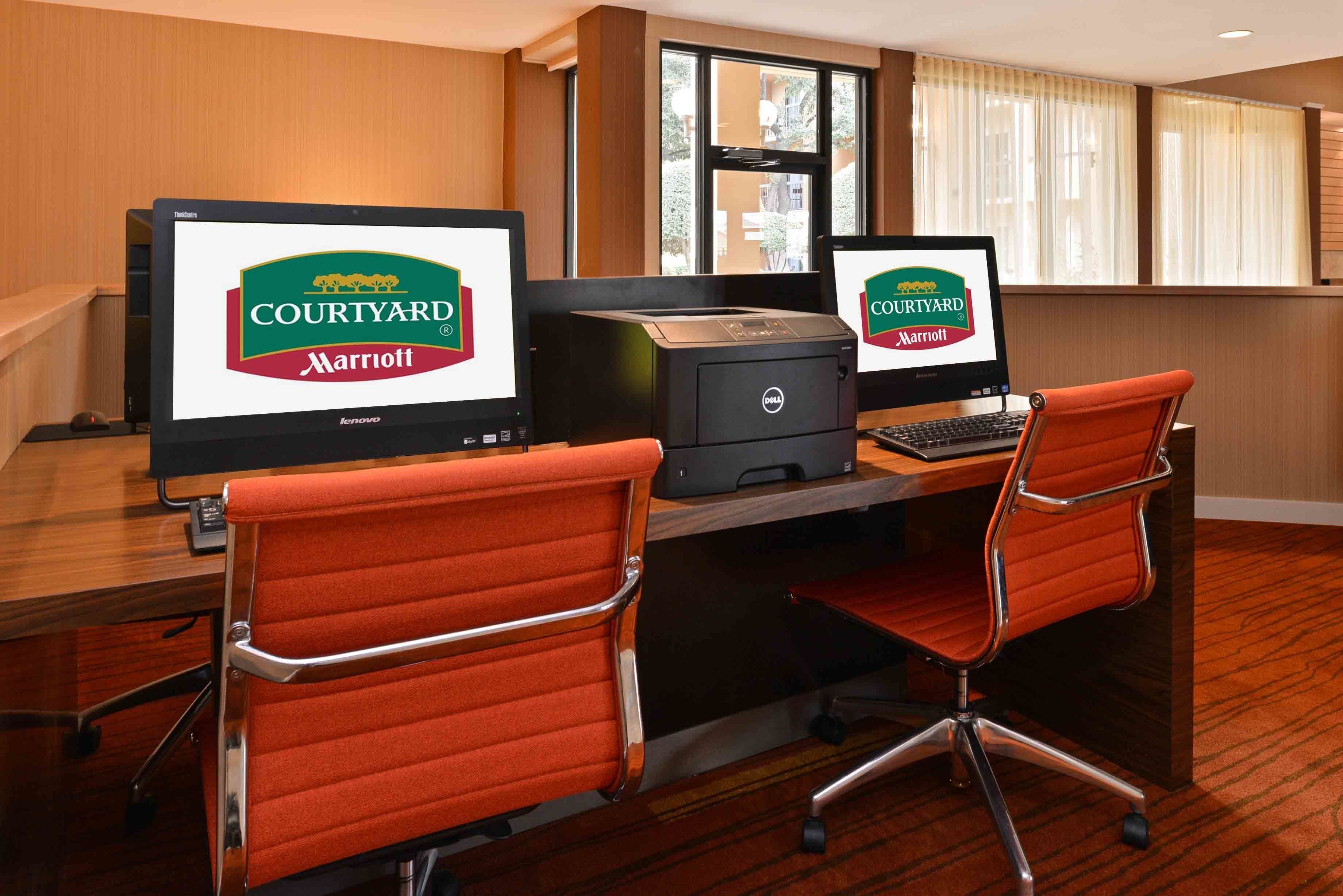 Una camera d'albergo con una scrivania, due monitor, una stampante e due sedie da ufficio arancioni.