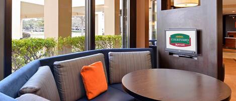 A Courtyard Marriott hotel room with a blue sofa, a round table, and a TV mounted on a wooden panel.
