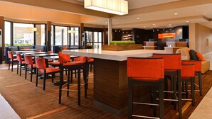 A modern bar area with high stools and a long counter, large windows, and a reception desk. - Courtyard by Marriott Dallas Northwest (Dallas)