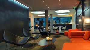 A modern lounge area with black and orange seating, a bar in the background, and a large illuminated wall.