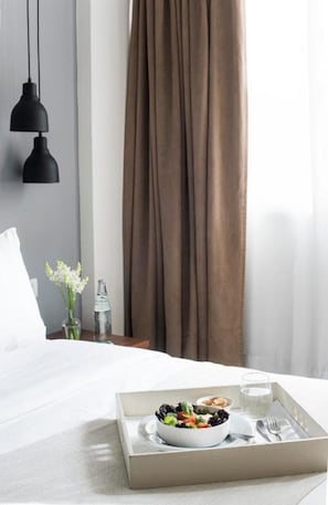 A hotel room with a bed, a tray with a bowl of salad, a bottle of water, and a glass of water.