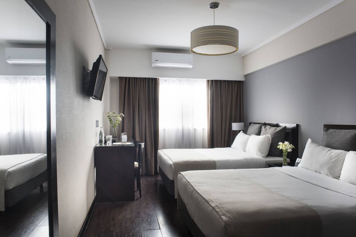 Une chambre d’hôtel avec deux lits, un bureau, une chaise, une télévision et un appareil de climatisation.