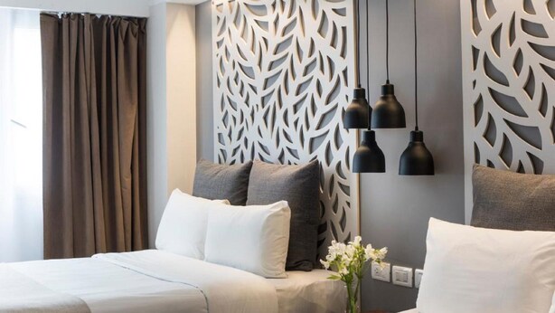 A hotel room with two beds, a decorative wall panel, and a vase with flowers.