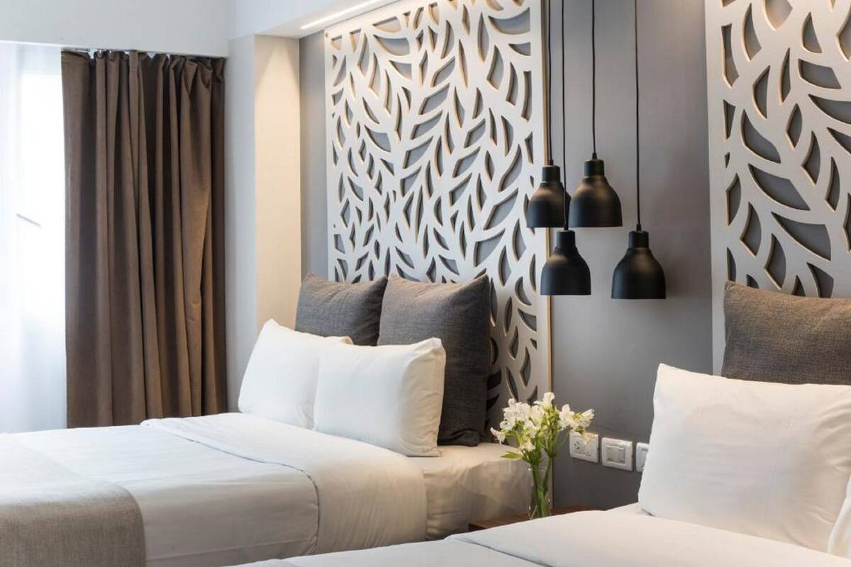 Une chambre d’hôtel avec deux lits, un panneau décoratif au mur et un vase rempli de fleurs.