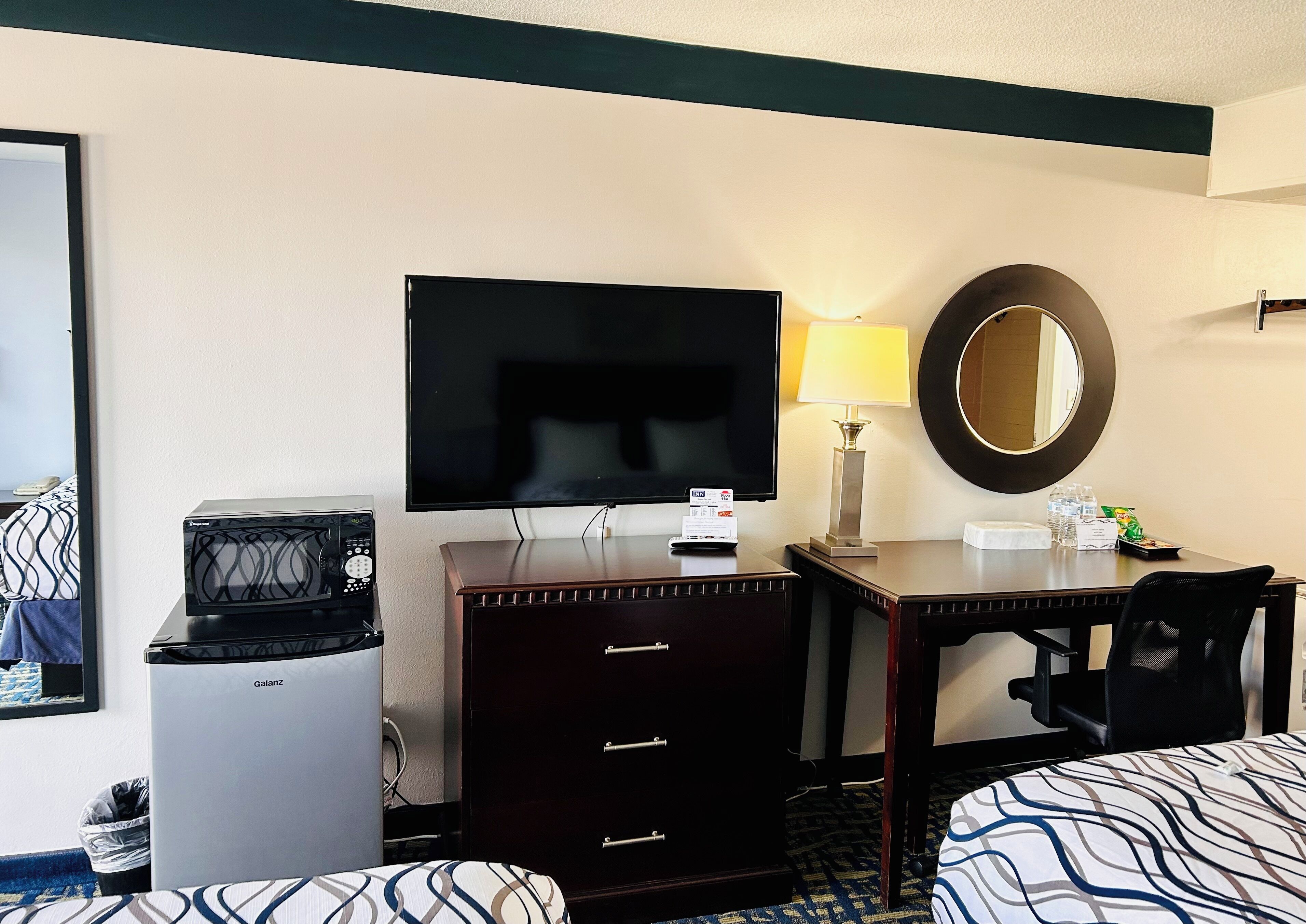 A hotel room with a bed, a desk with a computer, a television, a coffee maker, and a mirror.