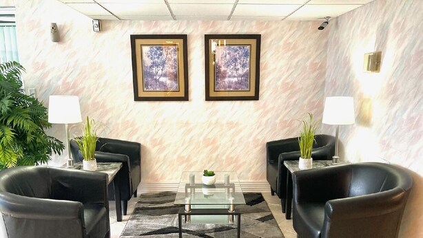 A lobby with a marble wall, two framed pictures, a glass coffee table, and black leather chairs. - Hospitality Inn (North Platte)