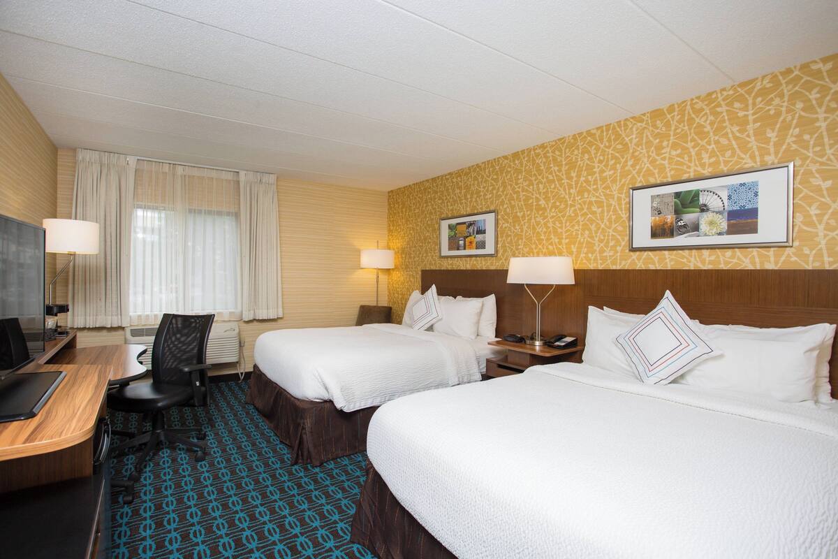 Une chambre d’hôtel avec deux lits, un bureau avec un ordinateur et une chaise.