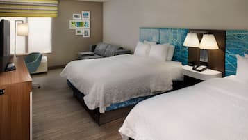 Habitación de hotel con dos camas, un escritorio, una silla, un televisor y obras de arte en las paredes.