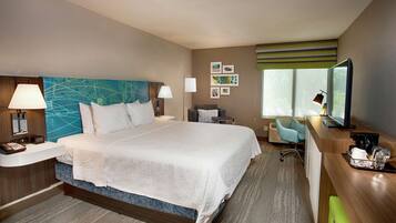 A hotel room with a large bed, bedside tables, a desk with a chair, a TV, and artwork on the walls.