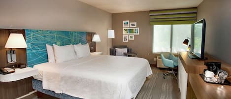A hotel room with a large bed, bedside tables, a desk with a chair, a TV, and artwork on the walls.