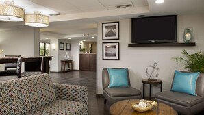 Un hall moderno con un sofá estampado, dos sillones, una mesa de centro de madera con objetos decorativos, un televisor de pantalla plana y cuadros enmarcados en la pared.