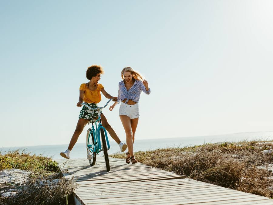 Due persone camminano su una passerella di legno con una bicicletta, con vista sulla spiaggia.