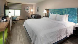 Una habitación de hotel con una cama grande, un escritorio con computadora, una silla, una lámpara y una pared decorada con cuadros.