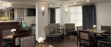 A hotel lobby with a bar area, seating arrangements, and a television mounted on the wall.