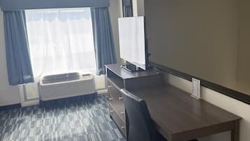 A hotel room with a desk, chair, air conditioning unit, and a large window with curtains.