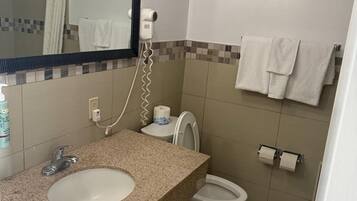 Een badkamer met een wastafel met granieten blad, een spiegel, een haardroger, een toilet en een handdoekhouder.