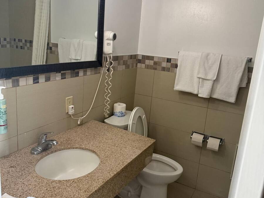A bathroom with a granite countertop sink, a mirror, a hairdryer, a toilet, and a towel rack.