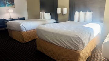 A hotel room with two beds, a desk, a chair, a lamp, and a painting on the wall.