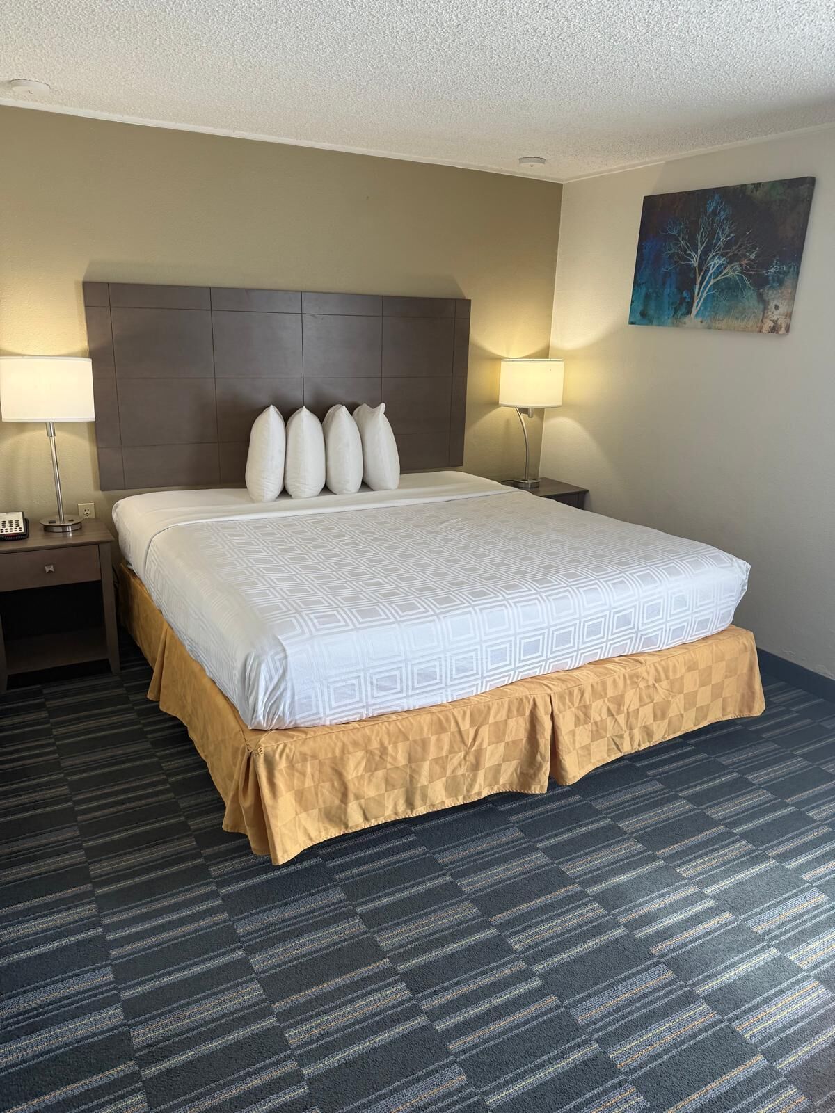 A hotel room with a large bed, two bedside tables, a headboard, and a painting on the wall.