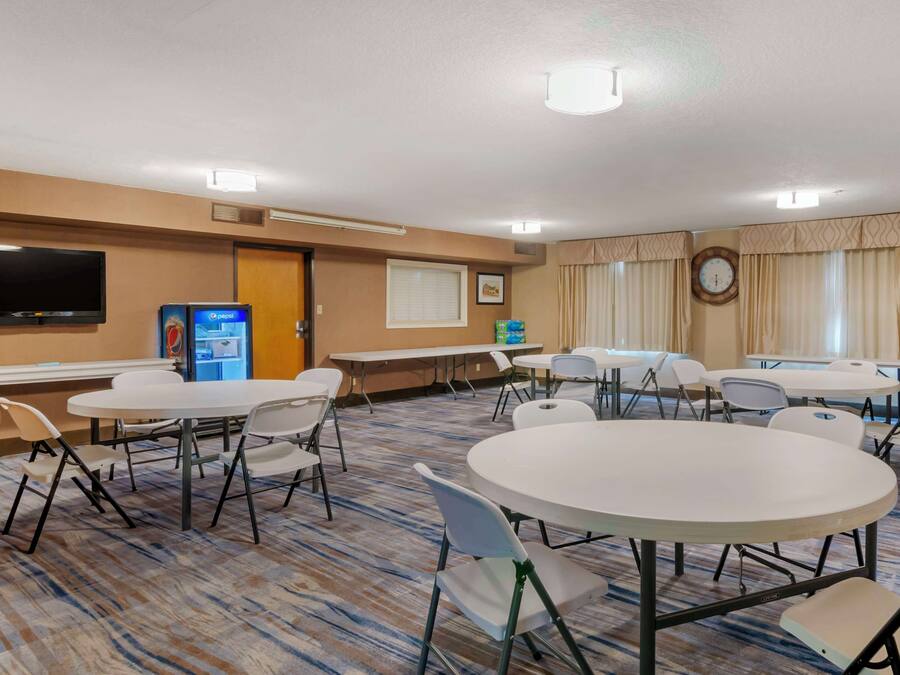 A hotel room with a large flat-screen TV, multiple tables and chairs, a clock, and a window with curtains.