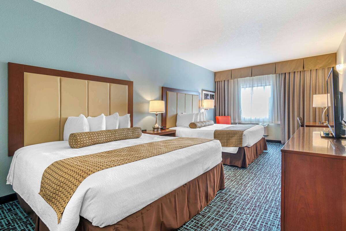 A hotel room with two beds, a desk, and a television.