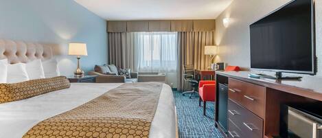 A hotel room with a large bed, a desk with a chair, a television, and a minibar.