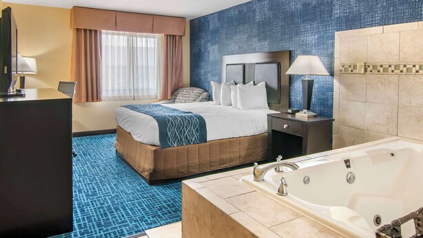 Una habitación de hotel con una cama grande, un baño independiente con bañera y un escritorio con silla.