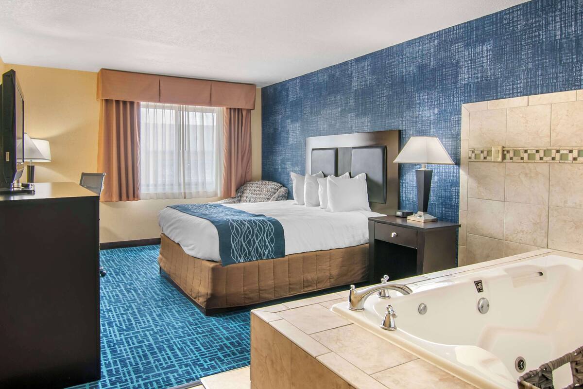 A hotel room with a large bed, a separate bathroom with a bathtub, and a desk with a chair.