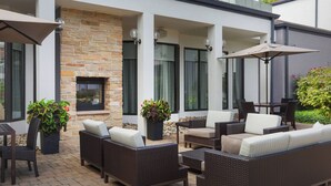 Un patio al aire libre con mobiliario de mimbre, chimenea de piedra y plantas en macetas.