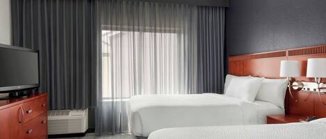 Habitación de hotel con dos camas, un televisor, un aparador y una ventana con cortinas.