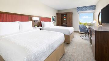 A hotel room with two beds, a desk, a chair, a TV, and a large window with a view.