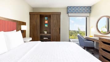 Hotelkamer met een groot bed, een bureau met stoel, een garderobe, een spiegel en uitzicht op groen.