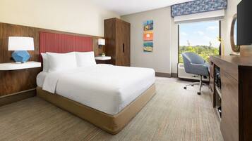 A hotel room with a large bed, a desk with a chair, a television, and artwork on the wall.