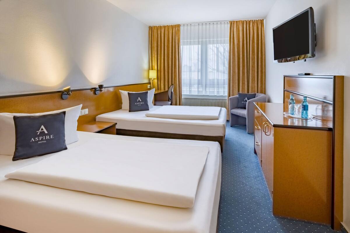 A hotel room with two beds, a desk, a chair, a TV, and a window with curtains.
