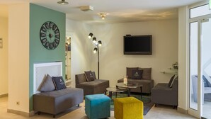 A modern living room with a large wall clock, multiple sofas, a coffee table, and a flat-screen TV. - Aspire Frankfurt Airport, Trademark Collection by Wyndham (Ruesselsheim)